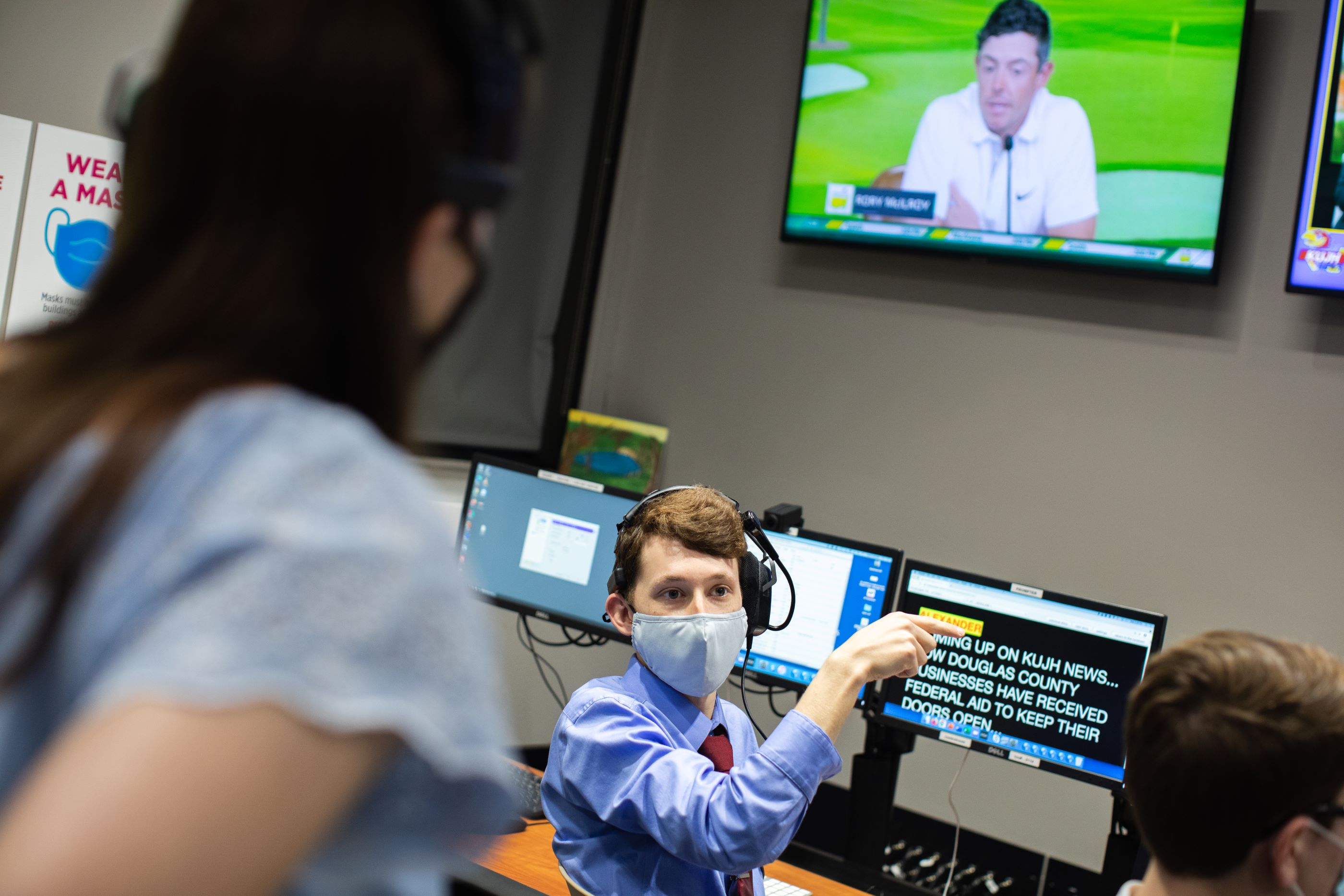 KUJH student sits at a computer and directs others