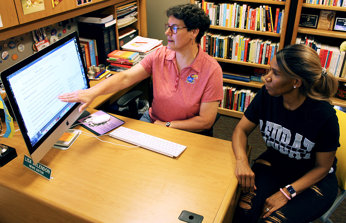 Instructor and student sitting at a desk collaborating on editing a document on a large display monitor