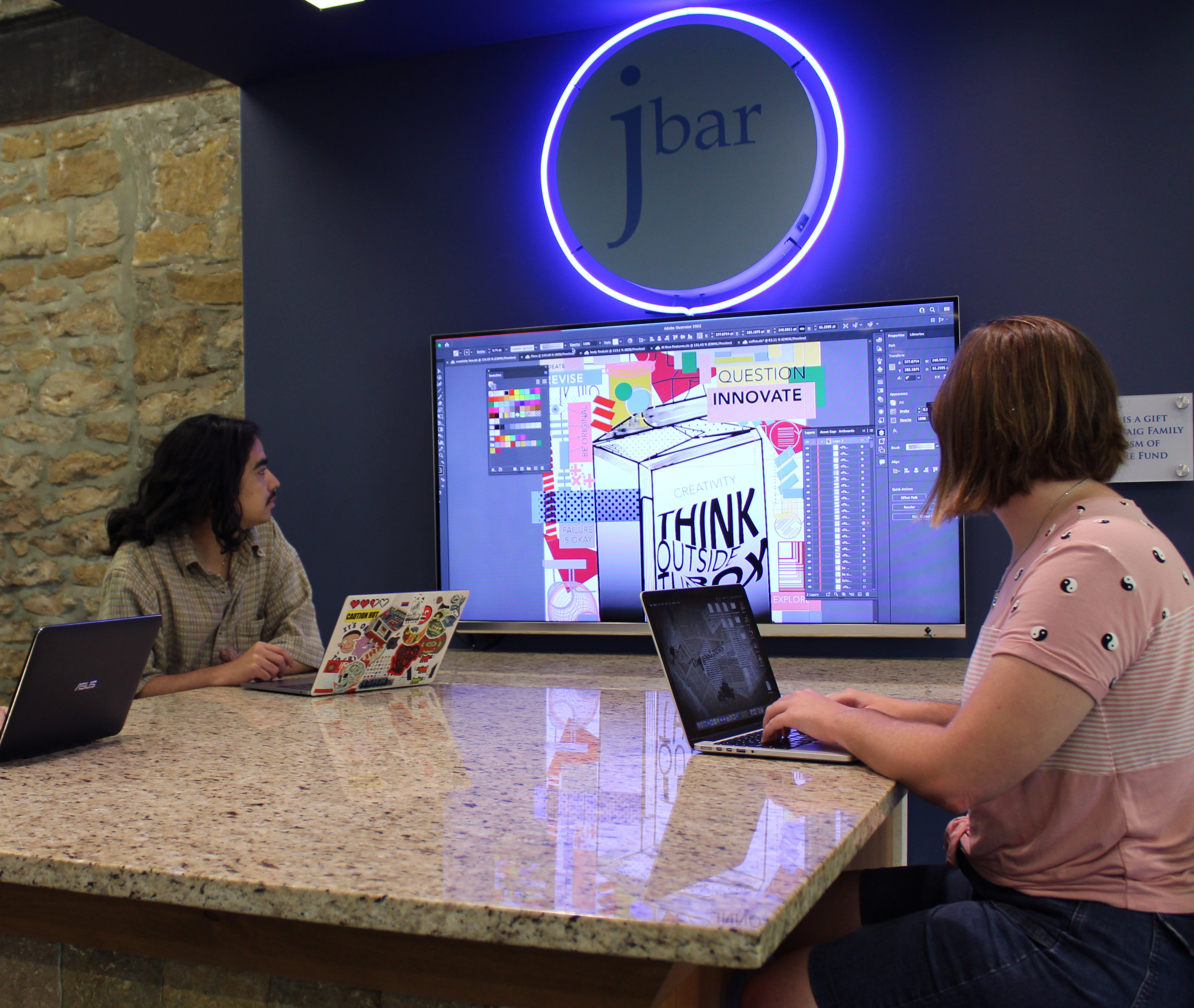 Students with laptops sitting at a table with a display screen learning Adobe Illustrator
