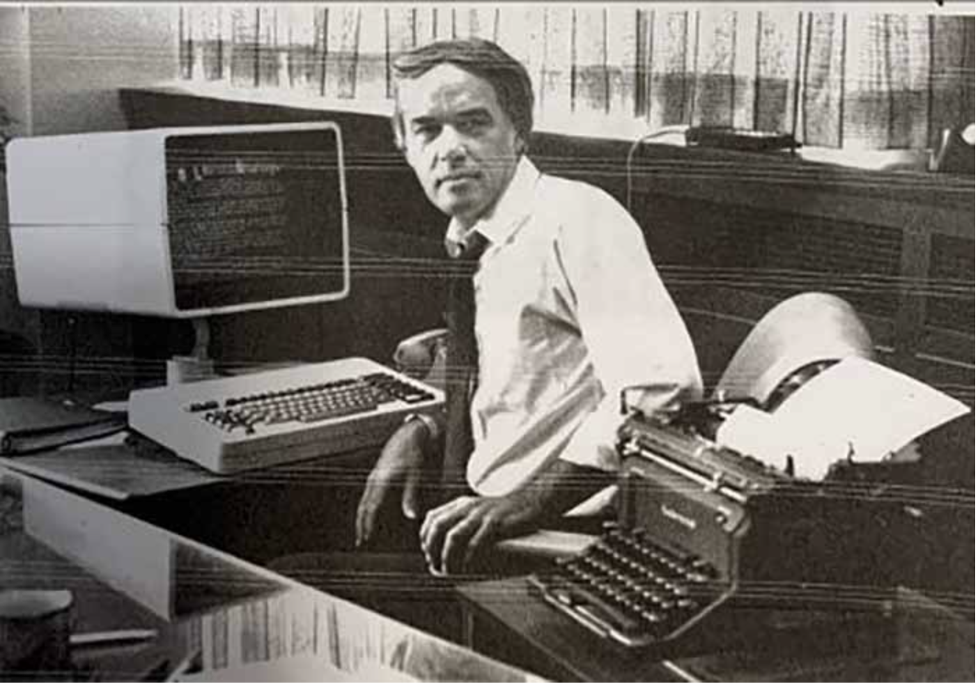 Buzz Merritt pictured at his desk with two generations of newspaper technologies