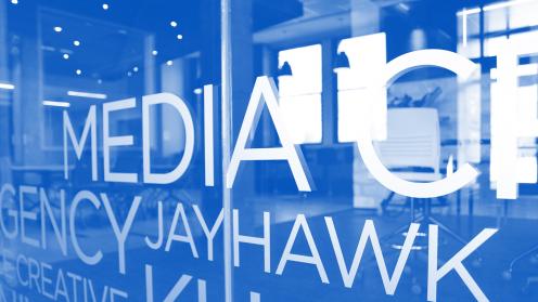 Glass wall that says Media and Jayhawk on it; photo is tinted blue